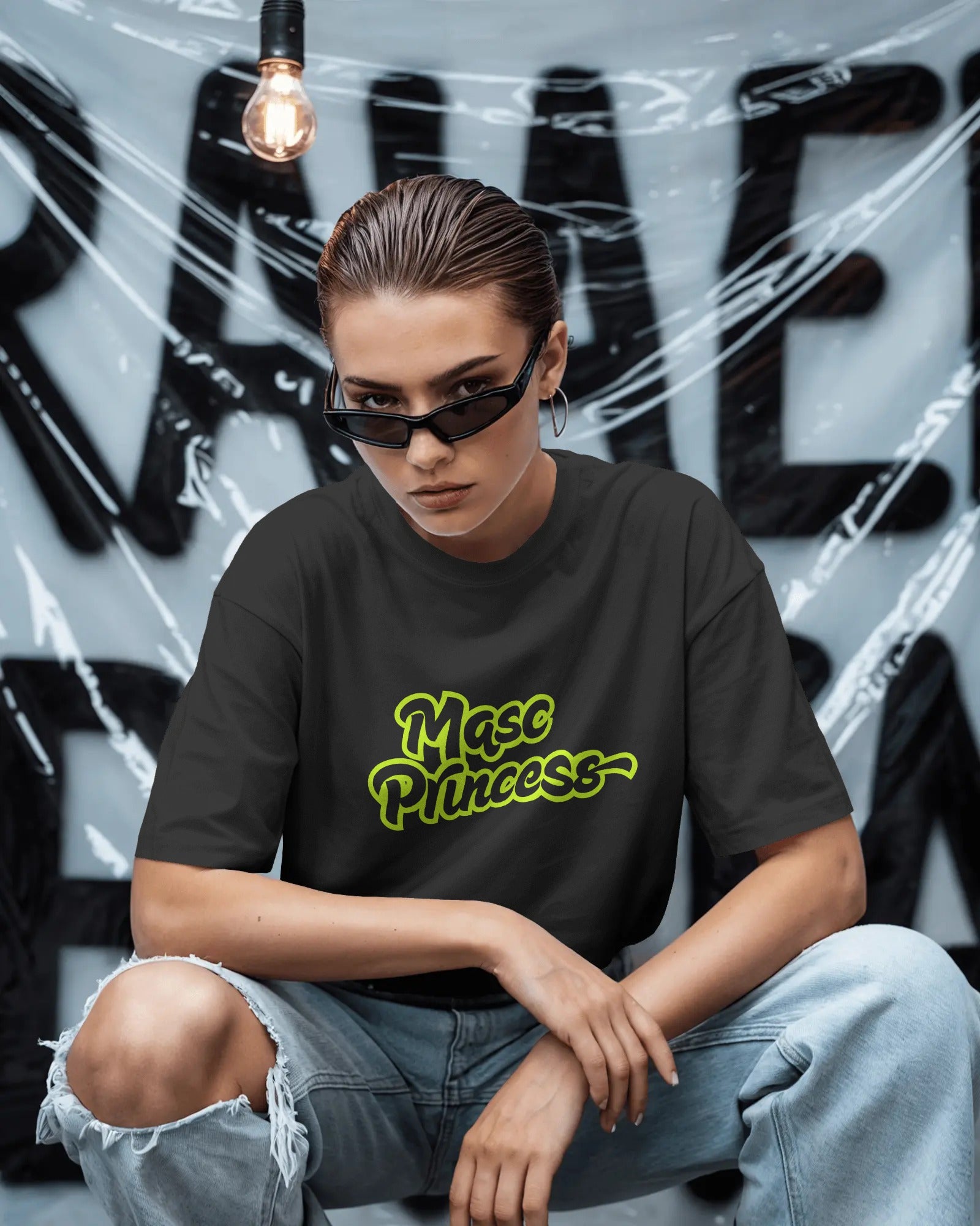Female model wearing black Masc Princess oversized t-shirt with neon green slogan, styled with ripped jeans and sunglasses, queer streetwear fashion