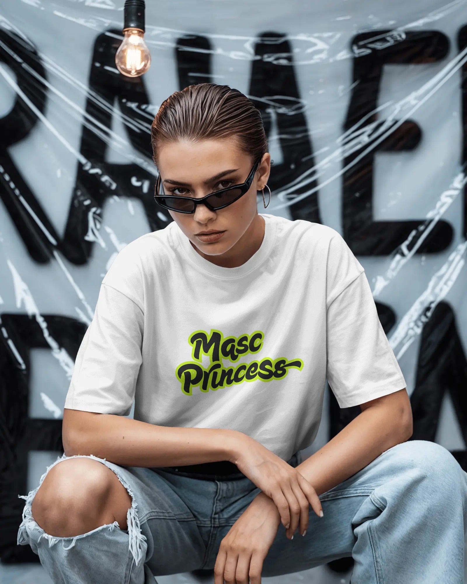 Female model wearing black Masc Princess oversized t-shirt with neon green slogan, styled with ripped jeans and sunglasses, queer streetwear fashion