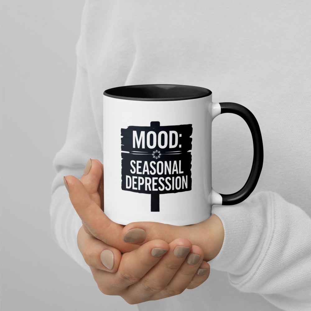 Mug with 'MOOD: Seasonal Depression' text held by a person against a plain background