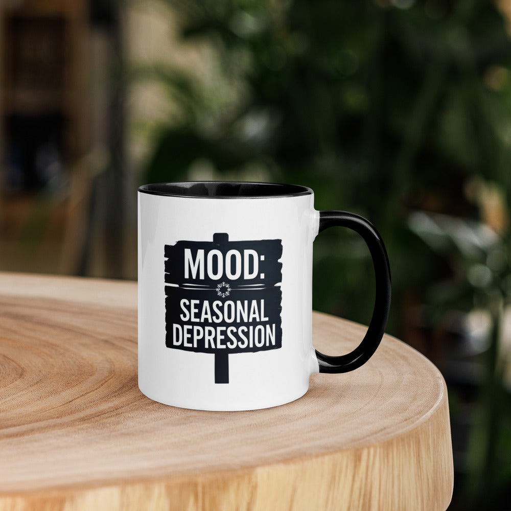 Mug with 'MOOD: SEASONAL DEPRESSION' text on a wooden surface with a blurred background