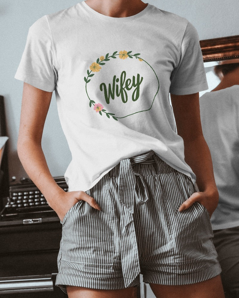 Person wearing a white t-shirt with 'Wifey' and floral design, paired with striped shorts.