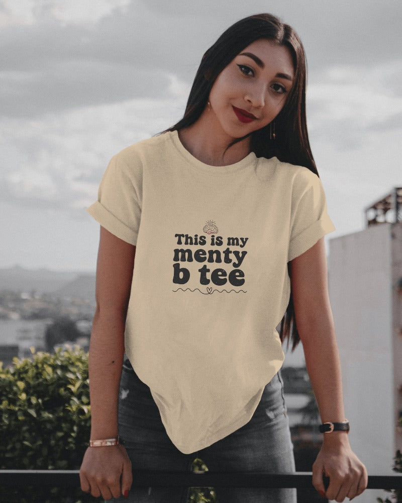Woman wearing a beige t-shirt with text, standing on a rooftop with a cityscape background